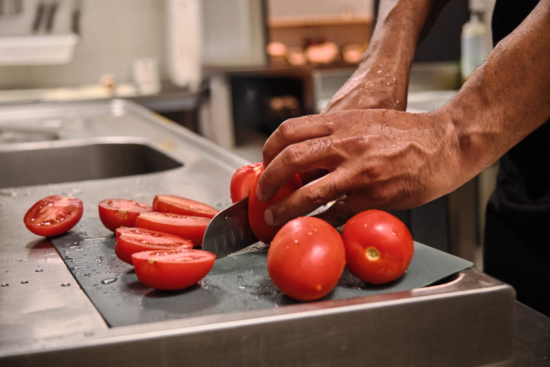 Manos cortando tomates frescos sobre tabla